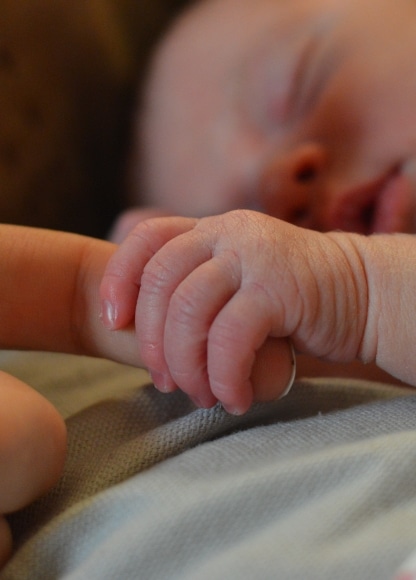 Newborn holding her caretaker's hand